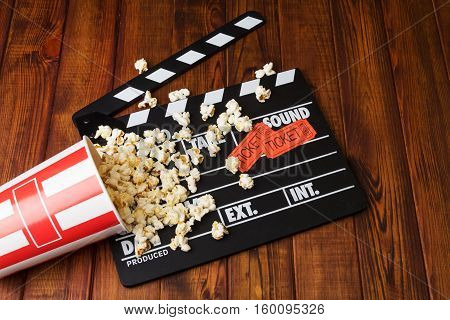 Loose popcorn, striped box, movie tickets and movie clapper on a wooden background