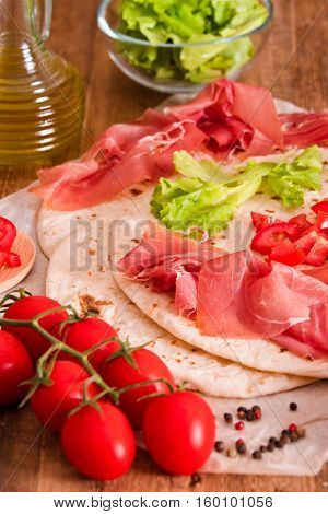 Piadina with ham and lettuce on wooden table.