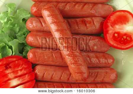 salsichas grelhadas, servidas no prato verde com salada e tomate