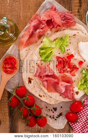 Piadina with ham and lettuce on wooden table.