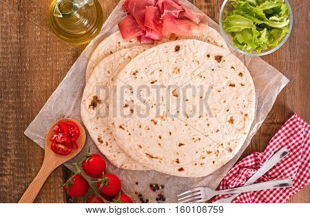 Piadina with ham and lettuce on wooden table.