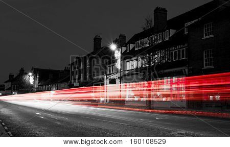 Traffic passing through a village in a monochrome filter with single red and white light trails