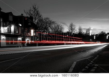 Red and white light trails through a village at twilight
