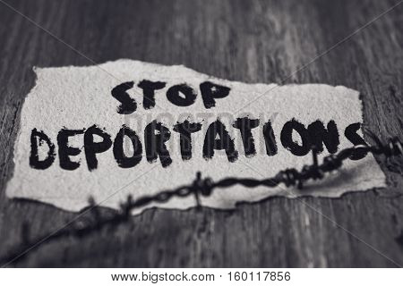 closeup of a barbed wire and a piece of paper with the text stop deportations handwritten in it on a rustic wooden surface