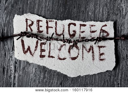 closeup of a barbed wire and a piece of paper with the text refugees welcome handwritten in it on a rustic wooden surface