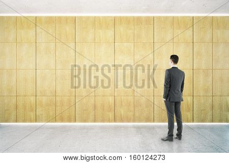 Thoughtful businessman in empty interior with blank wooden wall. Mock up 3D Rendering
