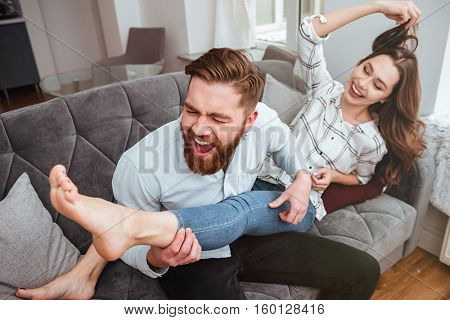 Loving couple sitting together on sofa. Man imagined that he play in girl's leg like at the guitar.