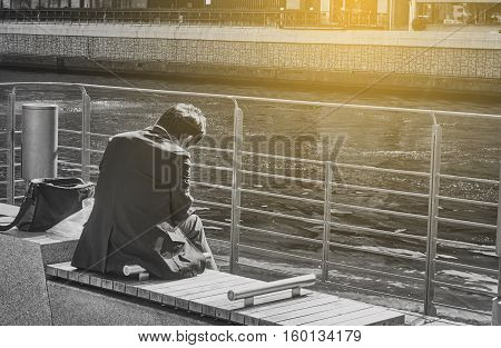 A sad business man is sitting in the public park. Sad and lonely man. Picture in black and white background. Artificial light was added at the top right corner for 'HOPE concept'.