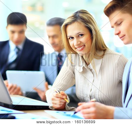 Smiling businesswoman posing while colleagues talking together in bright office
