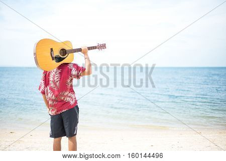 Handsome man playing classic guitar sitting on the beach in vacations