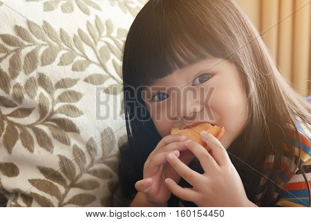 asian child or little girl enjoy eating a custard cake in the room with backrest pillow and sunlight