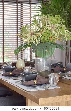 Big beautiful vase with green flower setting with modern dining set on wooden table