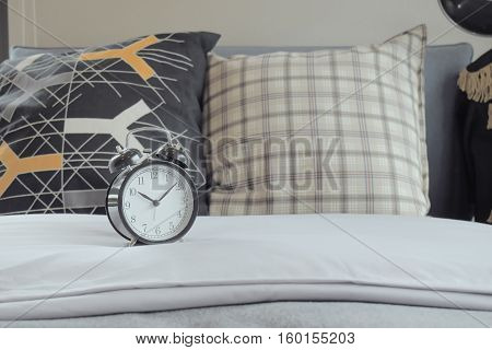 Classic Style Clock On White Linen And Grapic Pattern Pillows On Bed