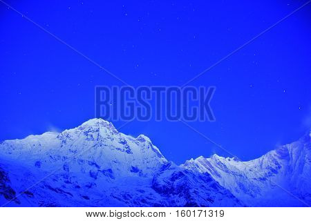 Before sunrise from Annapurna Base Camp (ABC) Trekking on the trail in the mountains. Sport girl with backpack travels in Himalayas. Nepal trek to ABC. Female traveler near Annapurna Base Camp. Snow and rocks winter severe landscape for background