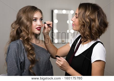 Makeup process, makeup artist colors model at salon. Portrait of two beautiful women