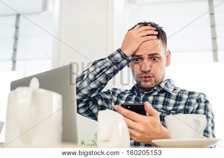 Worried shoked man looking on laptop at cafe.