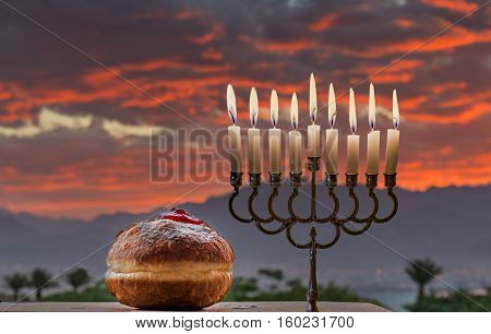 Jewish menorah with candles and sweet donuts are traditional symbols for Hanukkah holiday. Selective focus