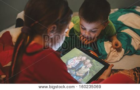 Little brother and sister sitting in pajamas using a digital tablet on Christmas Eve