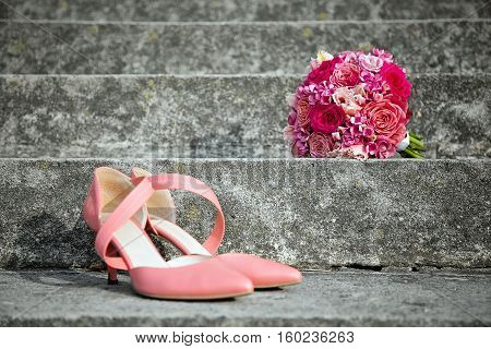 pink wedding shoes and wedding bouquet placed outdoor on a stairs bridal accessories close-up