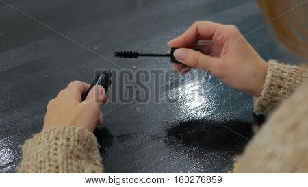 Woman opening new mascara, close up shot. Black table, makeup room. Beauty and make up concept