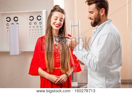 Ophthalmologist giving try-on tool for vision check to the young female patient in front of the eye chart in the cabinet. Eye doctor with patient in the clinic