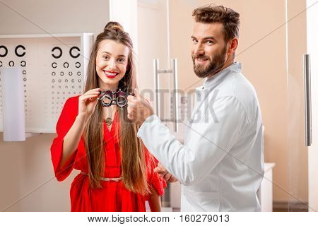 Ophthalmologist giving try-on tool for vision check to the young female patient in front of the eye chart in the cabinet. Eye doctor with patient in the clinic