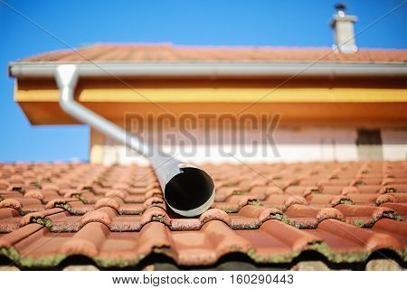 Detail photo of roof with a water spout and chimney.