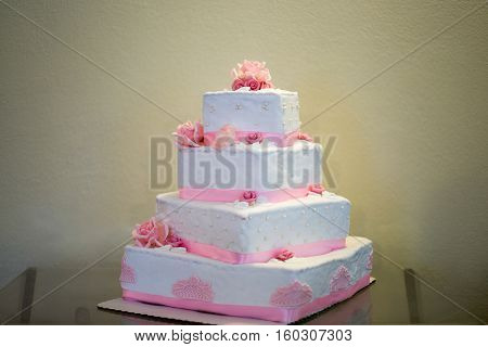 White storey wedding cake with pink edible marzipan flowers and pink decorative ribbon. Cake has four tiers square shape.