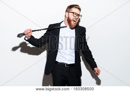 Business man in glasses and suit pulls his tie with open mouth and looking aside. Isolated gray background