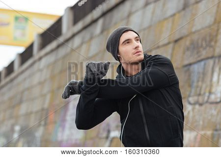 Hansome young man in hat and gloves standing and exercising outdoors