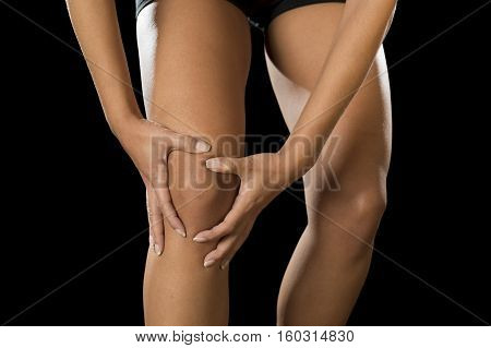 cropped close up view young sport woman holding injured knee suffering pain in ligaments injury or pulled muscle isolated on black background in fitness accident and body health care