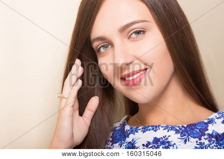 Closeup picture of beautiful model woman's face. Pretty lady looking at camera, smiling abd touching her brown hair.