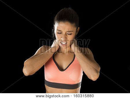 young attractive hispanic fitness woman touching and grabbing her neck and upper back suffering cervical pain isolated on black background in sport injury and body health care concept