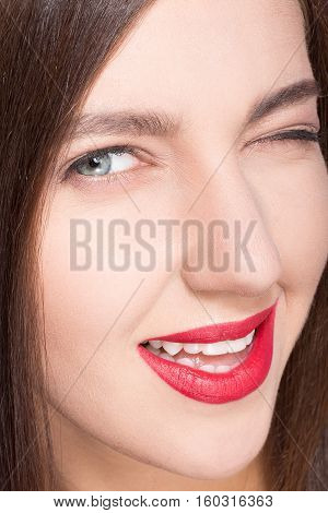 Face of model woman with clean skin and red lips. Professional model toothy smiling for camera and winking to photographer. Cosmetics concept. Skincare concept.