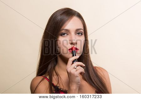 Young model woman doing makeup with lipstick isolated on white. Pretty lady with brown hair holding red colored lipstick in front of her.
