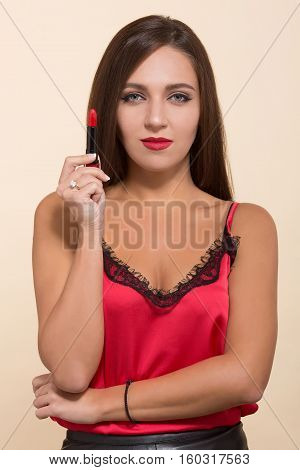 Portrait of young model woman holding red lipstick and looking at camera. Fashion lady doing makeup isolated on white background.