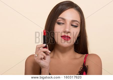 Lady holding red lipstick and looking at it. Briwn haired woman doing makeup isolated on white backgroun. Closeup concept. Cosmetics concept.