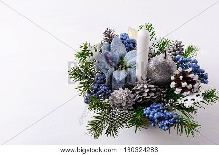 Christmas background with candle and blue silk poinsettias. Artificial Christmas flower arrangement with pine cones and fir branches. Christmas table centerpiece. Copy space.