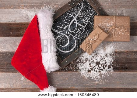 Christmas decoration with place for greeting on chalk blackboard. Santa Claus hat and gift boxes