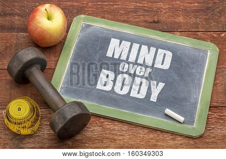 mind over body  concept -  slate blackboard sign against weathered red painted barn wood with a dumbbell, apple and tape measure