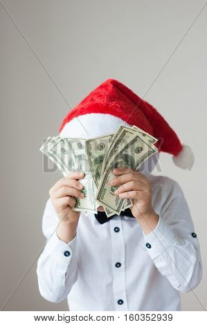 kid in Santa hat holding dollars hiding his face