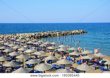 PANORMOS, CRETE - SEPTEMBER 15, 2016 - Tourists relaxing on the sandy beach with views towards the breakwater and sea Panormos Crete Greece Europe, September 15, 2016.