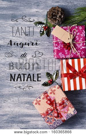 high-angle shot of some cozy christmas gifts on a rustic wooden surface and the text text tanti auguri di buon natale, merry christmas written in italian