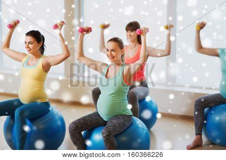 pregnancy, sport, fitness, people and healthy lifestyle concept - group of happy pregnant women with dumbbells exercising on stability balls in gym over snow