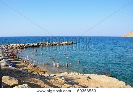PANORMOS, CRETE - SEPTEMBER 15, 2016 - Tourists relaxing on the sandy beach with views towards the breakwater and sea Panormos Crete Greece Europe, September 15, 2016.