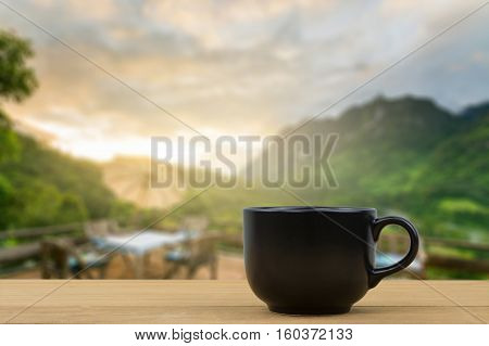 black coffee cup on wooden table over blurred image of beautiful dinner place and nice view over the mountain, Chiang Mai, Thailand