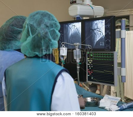 Monitors with scanner image of heart arteries and heartbeat during non-invasive surgery in hospital.