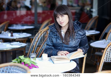 Dark-haired Beautiful Woman With Book In Parisian Street Cafe