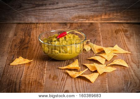 Guacamole dip and nacho chips on glass bowl.