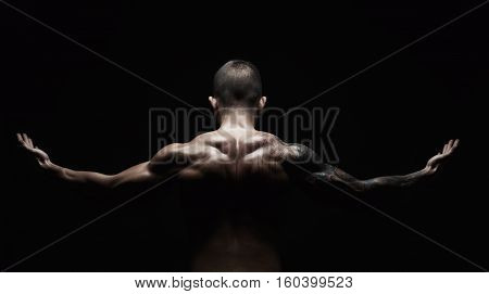 Unrecognizable man bodybuilder shows strong hands and neck muscles, athletic trapezius. Low key, studio shot on black background.